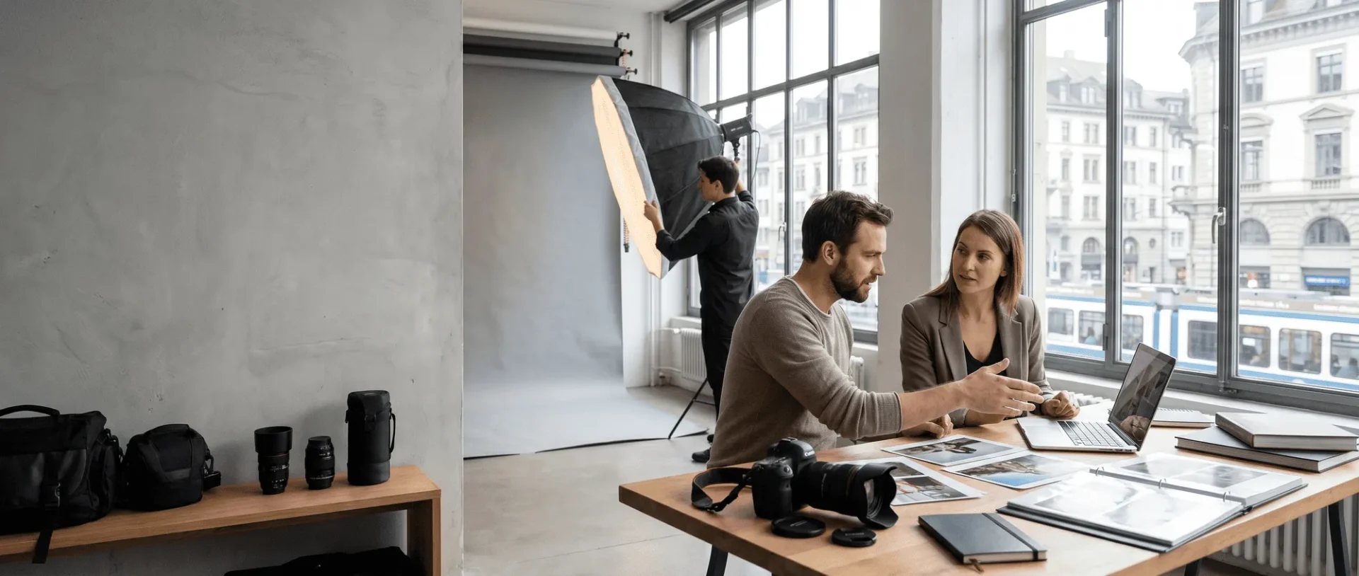 Fotostudio-Team arbeitet an Projekten; Kameraausrüstung, Laptop, Fotos; jemand richtet Beleuchtung ein.