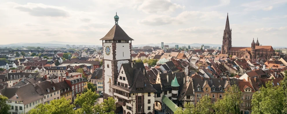 Panorama von Freiburg: Historischer Martinstor-Turm und der beeindruckende Freiburger Münster im Hintergrund unter blauem Himmel als Visualisierung für Online Marketing aus Freiburg.