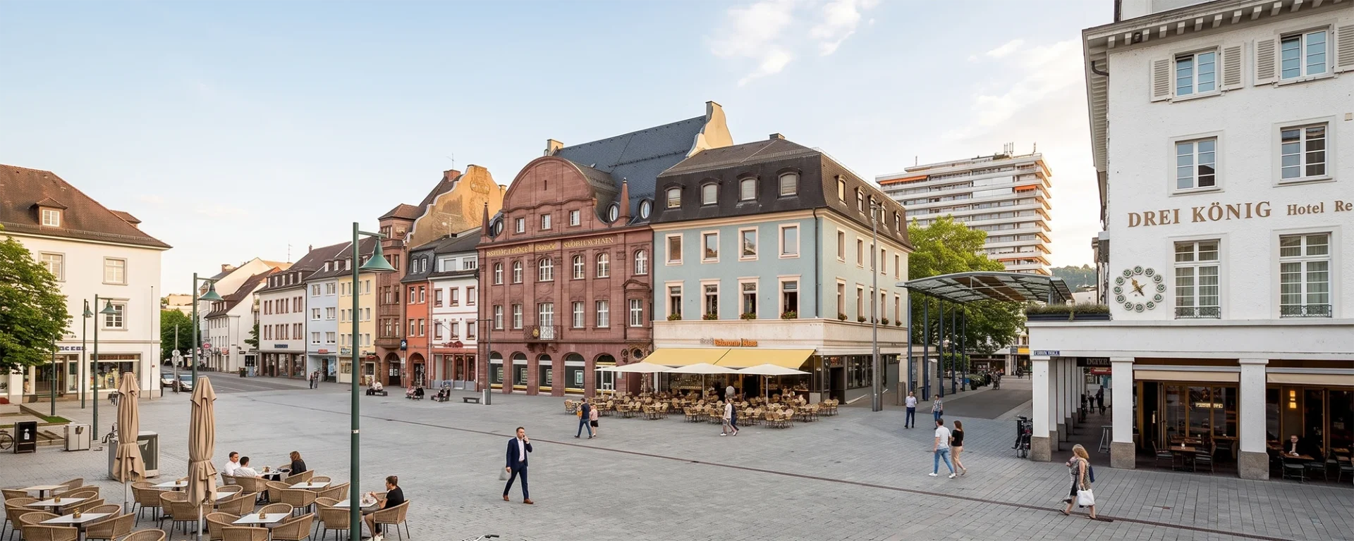 Marktplatz Lörrach mit historischen Gebäuden, Restaurant Drei König und weiteren Cafés und Menschen in der Innenstadt bei Tageslicht.